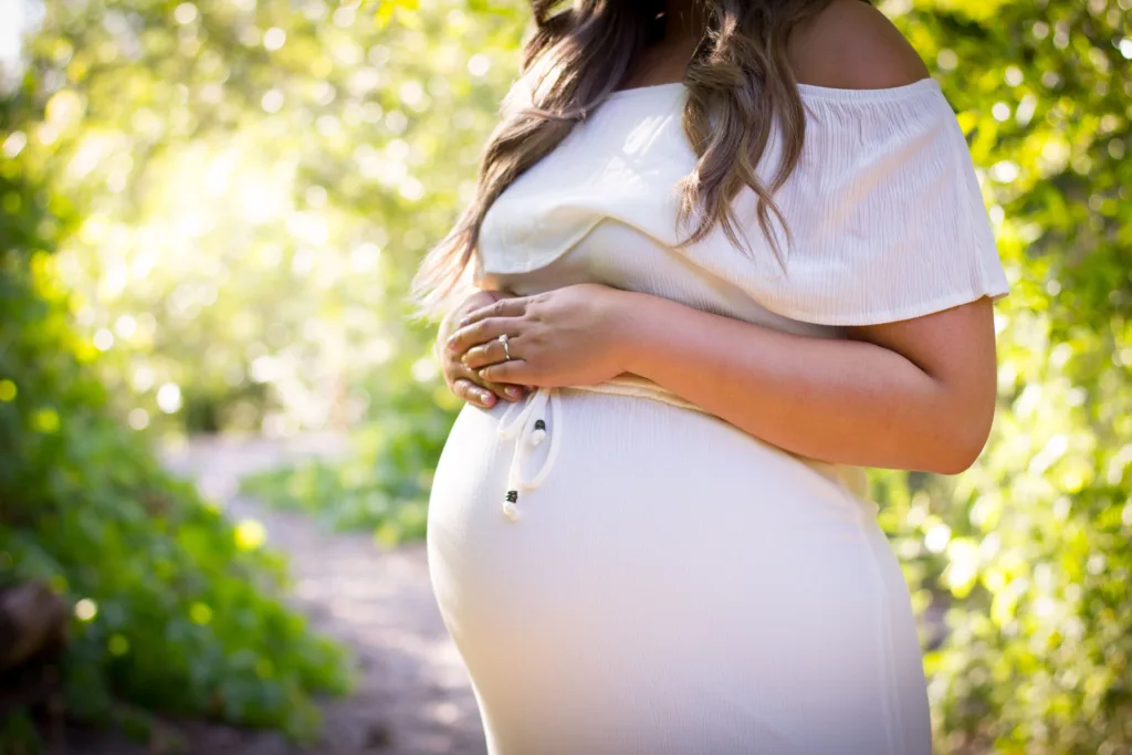 Pregnancy self-care, pregnant woman in white dress standing and holding her belly with two hands