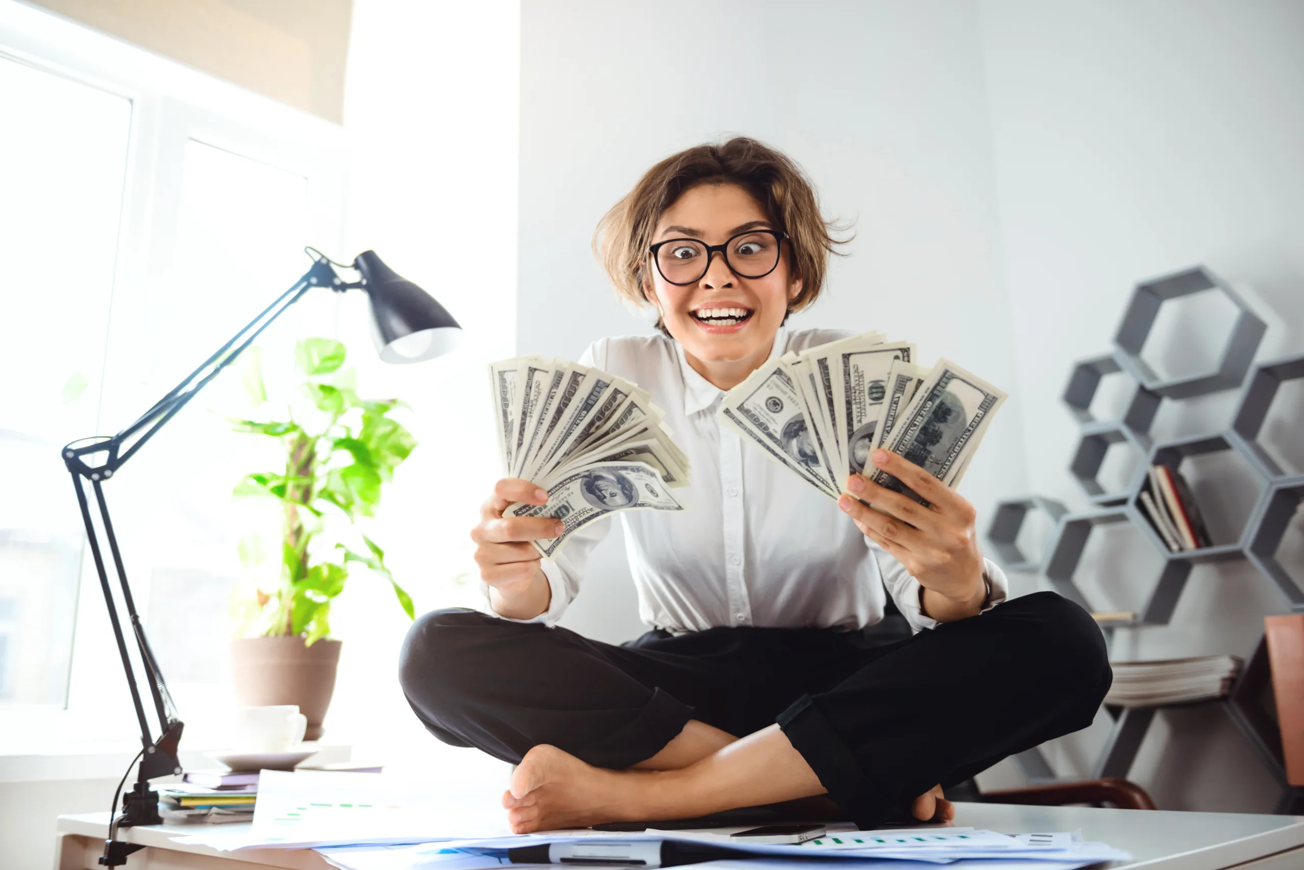Young beautiful businesswoman holding money, sitting on table at workplace. Money meditations